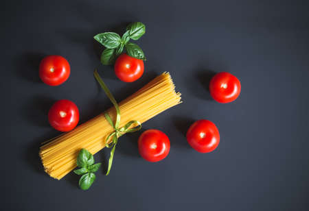 Raw spaghetti pasta with fresh tomatoes and basil leaves on dark background. Top view, copy space.の写真素材