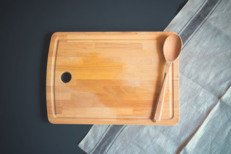 Wooden cutting board with wooden spoon on dark background
