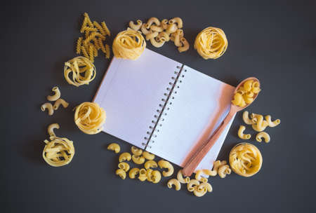 Notepad and raw pasta on dark background.の写真素材
