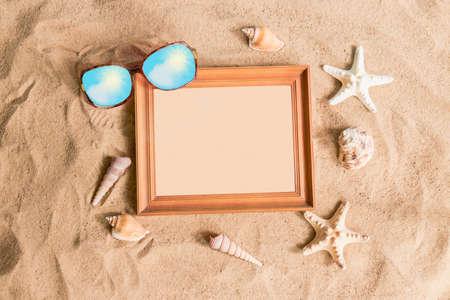 Wooden frame, sunglasses and seashells on sand beachの写真素材