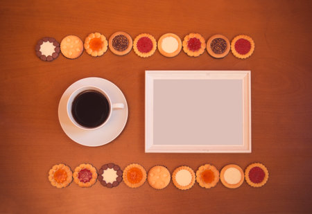 White frame, cup of coffee and assortment of mixed biscuits on rustic wooden background. Top view,...