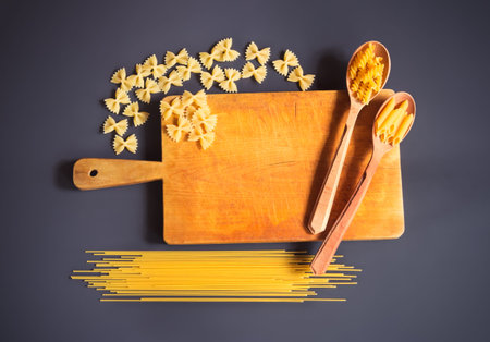 Cutting board and raw pasta on dark background.
