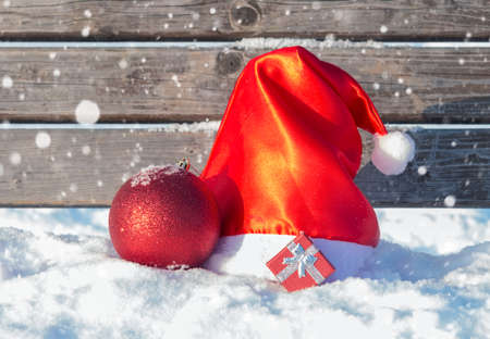 Santa hat with christmas decorations and gift on wooden surface with snowの写真素材