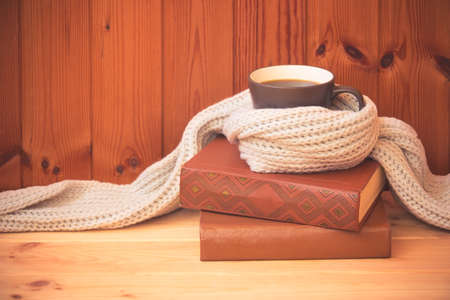 Mug of hot coffee wrapped in woolen scarf and stack of books. View with copy space.の写真素材