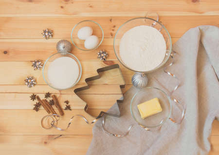 Cookie cutter in shape of christmas tree surrounded by flour, sugar, butter, eggs, spices and christmas decorationsの写真素材