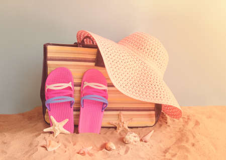 Flip flops, bag, summer hat and seashells on sand beach on blue backdrop. Summer holidays concept.の写真素材