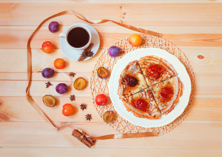 Cup of coffee, pancakes with homemade plum  jam, spices and fresh plums on wooden table. Top view.の写真素材