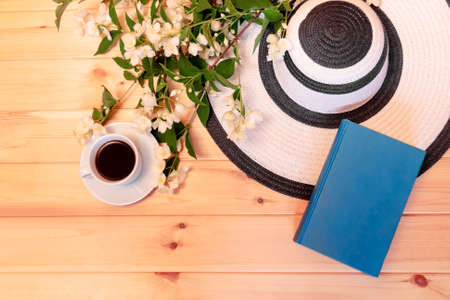 Summer hat, cup of coffee, book and jasmine flowers on wooden background. Top view. Summer rest concept.の写真素材