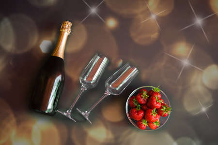 Bottle of champagne and two empty glasses on horizontal position and bowl of strawberries. Dark backgroundの写真素材