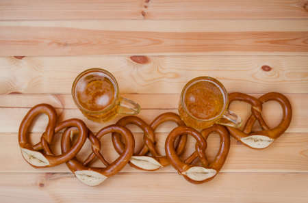 Two mugs with beer and freshly baked pretzels on wooden background. Top view with copy space.の写真素材