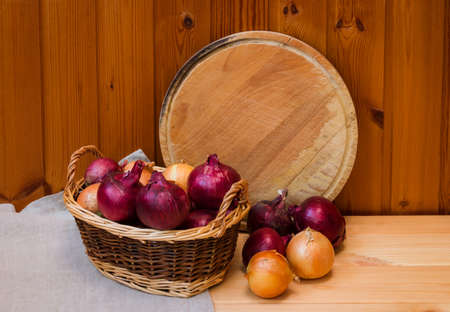 Colorful onions in basket and cutting board as copy space behind. Selective focus.の写真素材