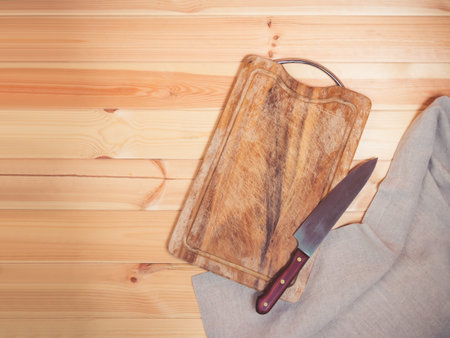 Empty wooden cutting board, kitchen knife  and napkin on rustic wooden background. Top view, copy...