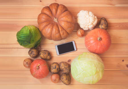 Fresh vegetables and smartphone on wooden background. Top view, copy space. Concept of digital recipe book and shopping list.の写真素材