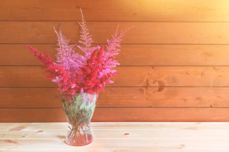 Red and pink beautiful astilbe flowers in glass vase on wooden table. Selective focus. View with copy space.の写真素材