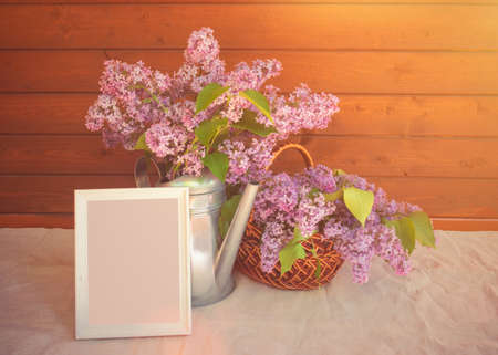 White frame with copy space for your text, watering can and basket with branches of lilac flower on tableの写真素材