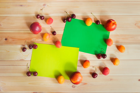 Cards for notes surrounded by ripe cherries, nectarines and apricots on wood. Summer fruit...