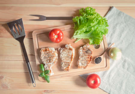 Grilling pork steaks,  salad leaves and fresh tomatoes on cutting board. Top view.の写真素材