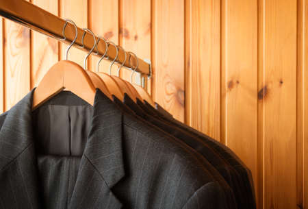 Row of men's suits on hanger. Wooden background. Selective focus. View with copy space.の写真素材