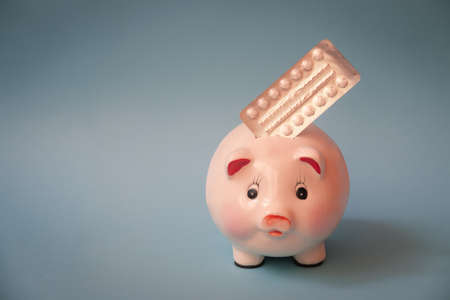 Piggy bank and pills in blister pack on blue  background. View with copy space.の写真素材