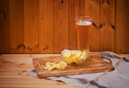 Glass of light  beer with potato chips on  wooden table. View with copy space.の写真素材