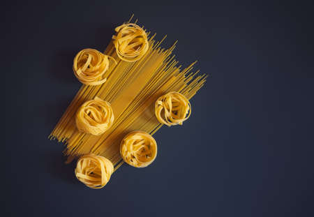 Raw pasta fettuccine and spaghetti on dark background. Top view, copy space.の写真素材