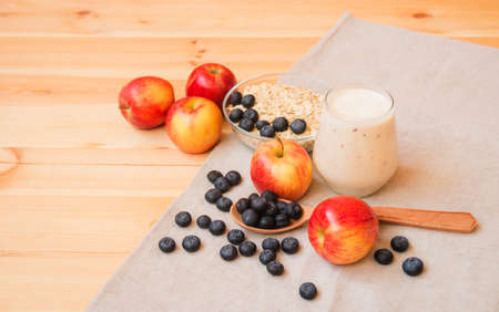 Glass of yogurt, apples, bilberries and  oat flakes in bowl on wooden table. Selective focus.の写真素材