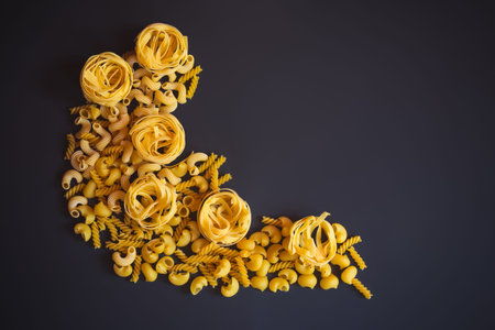 Border made of different kinds of raw pasta on dark background. Top view, copy space.