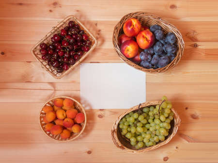 Wicker baskets full of ripe summer fruits on wooden table with empty card for your text.  Top view.の写真素材