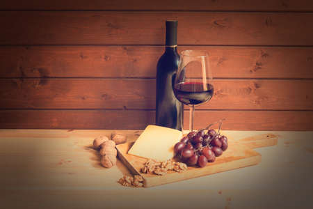 Glass of red wine, bottle of wine, parmesan cheese, walnuts and red grapes. Toned image. View with copy space.の写真素材