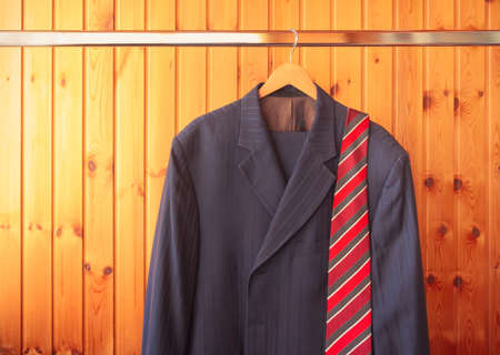 Men's suit and red striped tie on hanger on wooden background. View with copy space.の写真素材