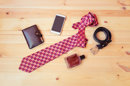 Stylish necktie, wallet, smartphone, perfume and rolled belt on wooden background. Top view, copy...
