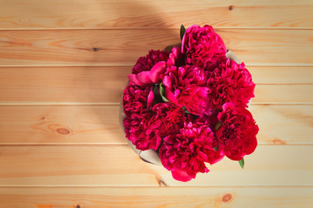 Beautiful red peony flowers in basket on wooden background. Top view, copy space.