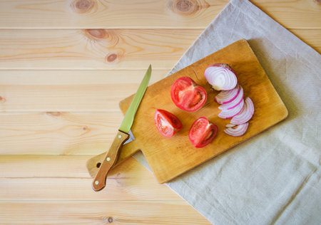 Cutting board, knife and cutted  tomato and purple onion on wooden background. Top view, copy space.