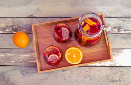 Red wine sangria with fruits in glasses and pitcher on wooden tray with oranges near. Top view.の写真素材