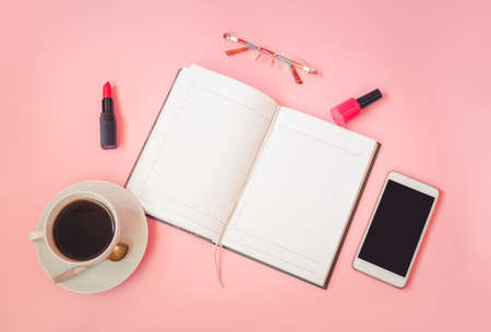 Cup of coffee, glasses, lipstick, nail polish, smartphone and diary on pink background. Top view, copy space.の写真素材