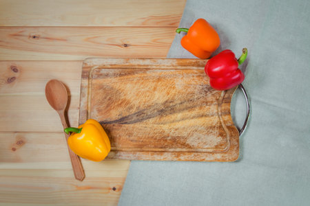 Cutting board and colorful fresh ripe peppers on wooden background. Top view, copy space.の写真素材