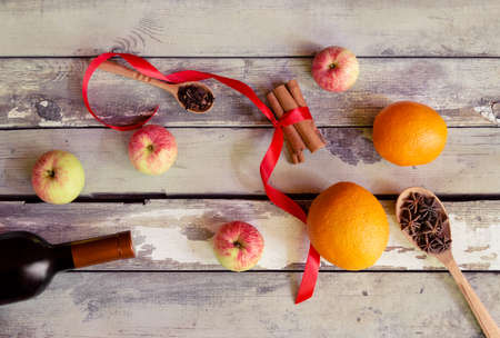 Mulled wine recipe ingredients. Bottle of red wine, oranges, cinnamon sticks, anise, cloves and apples on aged wooden background. Top view.の写真素材