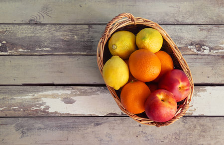 Basket with oranges, nectarines and lemons on aged wooden background. Top view, copy space.