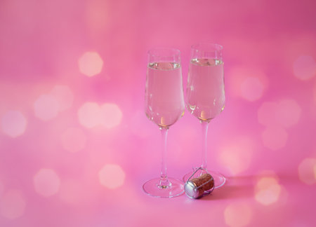 Two glasses of champagne and cork on pink background. View with copy space.