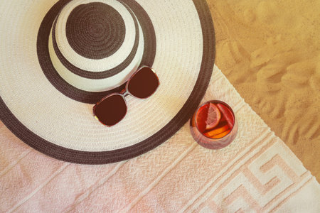 Large beach hat, sunglasses, glass of red wine sangria and towel on sand beach. Top view.