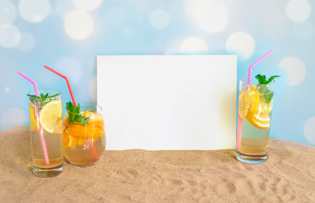 Empty card for your text and glasses of cold summer drinks with lemon and orange on sand beach.  Summer holidays concept. View with copy space.の写真素材