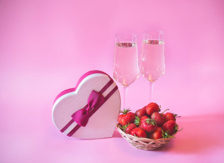 Two glasses of champagne, heart shape gift box and fresh strawberry on pink background. Selective...