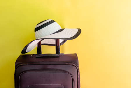 Brown suitcase and large beach hat on yellow background. View with copy space.の写真素材