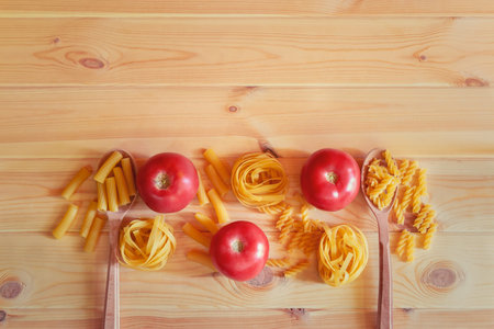 Border made of different kinds of raw pasta and fresh tomatoes on wooden background. Top view, copy...