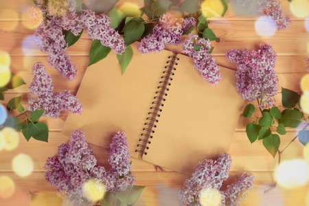 Empty notepad surrounded by fresh flowers of lilac on woodenの写真素材