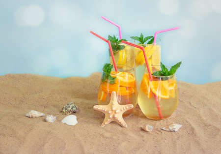 Cold summer lemonade and orange lemonade on sand beach. Starfish and seashells near. Selective focus. View with copy space.の写真素材