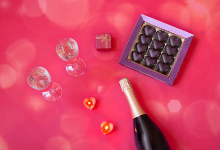 Romantic concept. Two glasses of champagne, bottle of champagne, box of chocolate, gift and heart shape candles on pink. Top view. Selective focus.の写真素材