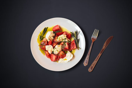 White plate with caprese salad with ripe tomatoes, mozzarella cheese, pesto sauce and olive oil on...