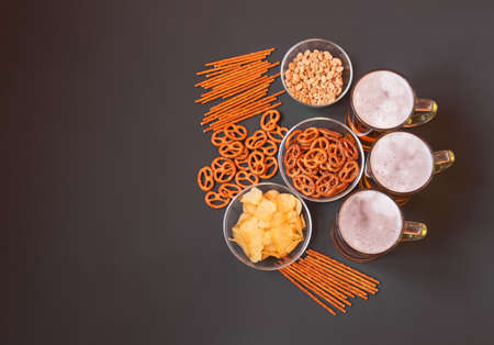 Mugs of beer with salted pretzels, salted straw, potato chips and peanuts on darkの写真素材