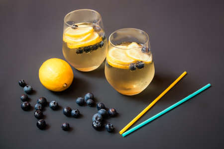 Glasses of summer lemonade with blueberries and lemon, blueberries, lemon and drinking straws near on dark surface. Selective focus.の写真素材